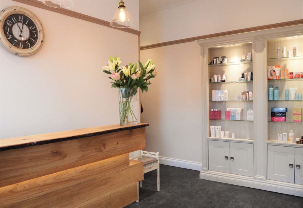 Clinic reception area with products on a shelving unit made of white painted wood, with glass shelves